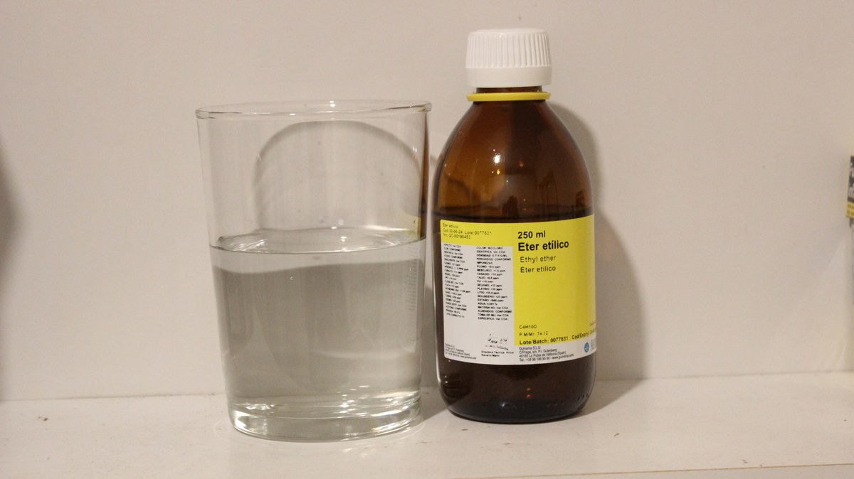 Vaso con l&iacute;quido transparente junto a un frasco &aacute;mbar de 250 ml etiquetado como &eacute;ter et&iacute;lico