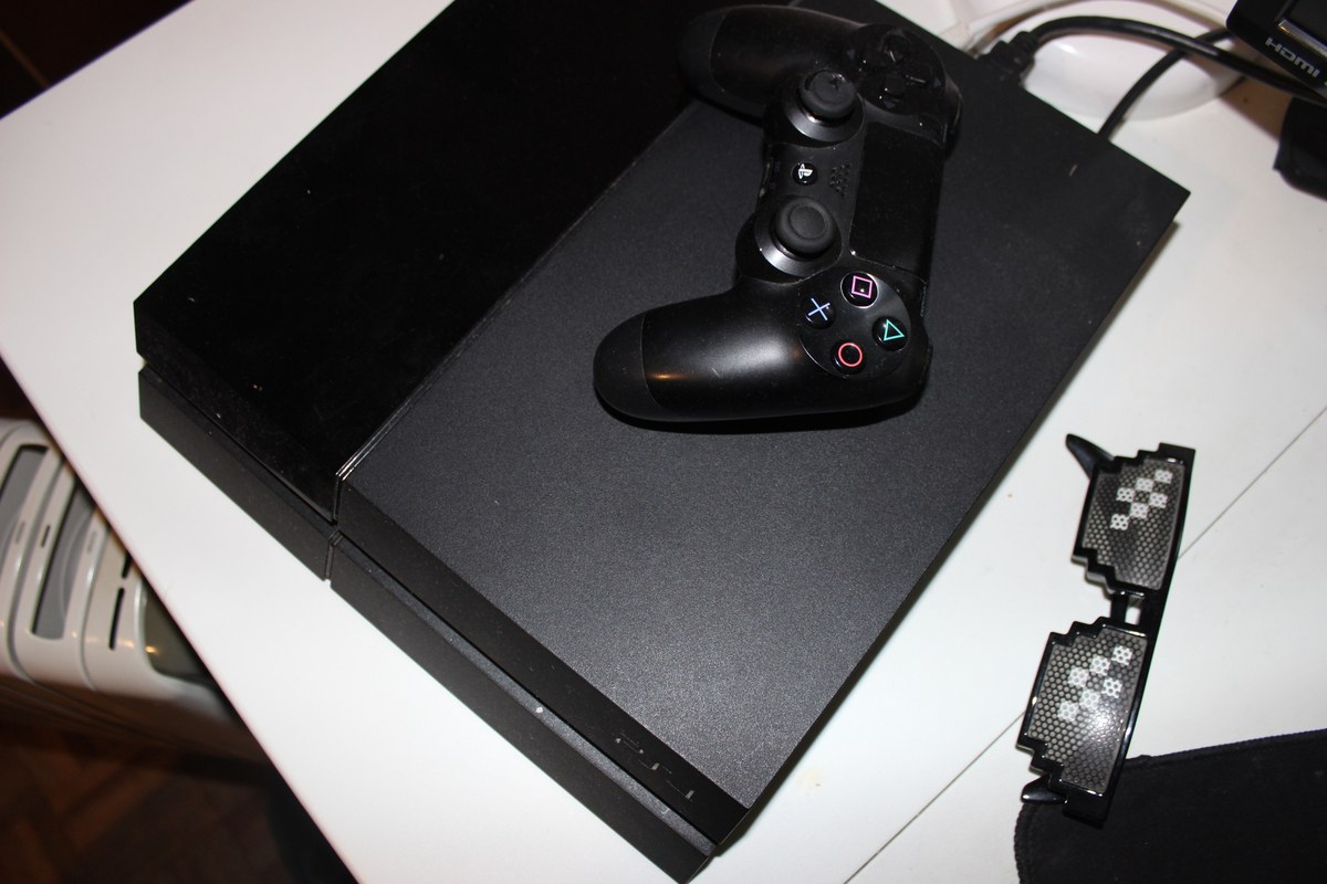 Consola negra con un mando encima y unas gafas de rejilla a un lado