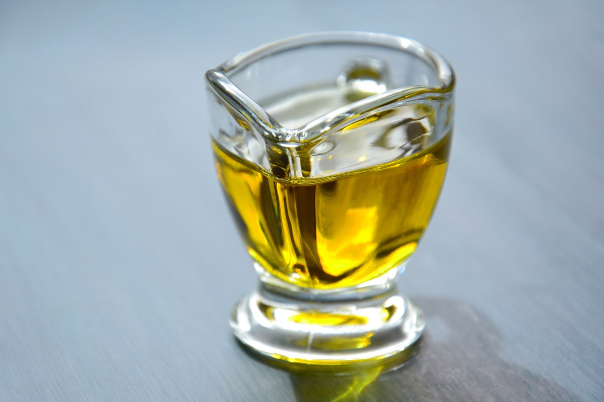 Peque&ntilde;a jarra de vidrio transparente llena de aceite dorado sobre una mesa gris