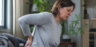 Persona con dolor cr&oacute;nico de espalda junto a medicaci&oacute;n analg&eacute;sica y hojas de cannabis en segundo plano
