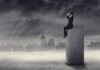 Cannabis, normas y control social Hombre con prismáticos sentado sobre un bloque, ante una ciudad industrial cubierta de humo y niebla