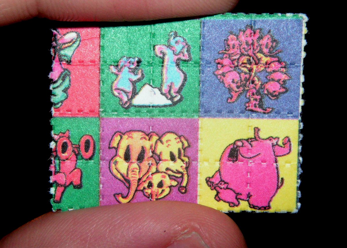 Pequeño papel secante con cuadros de colores y personajes de dibujos animados, sostenido entre dos dedos