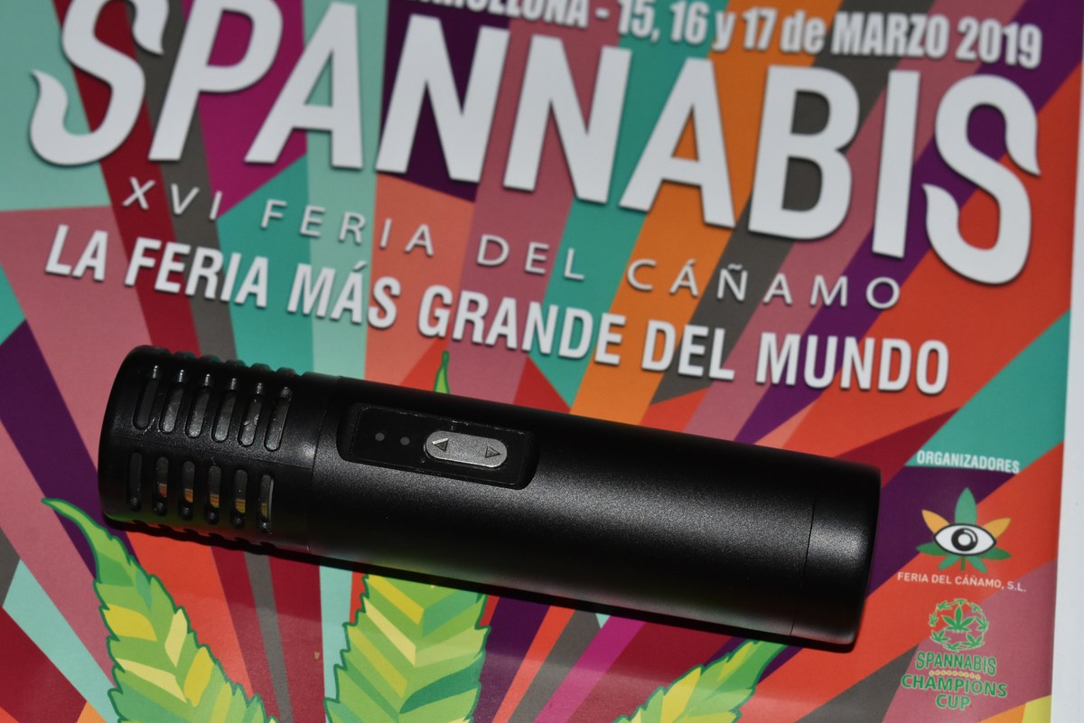 Vaporizador port&aacute;til negro sobre un cartel multicolor de una feria del c&aacute;&ntilde;amo