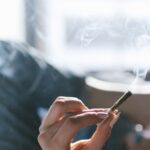 Una persona sostiene un porro encendido mientras permanece tumbada en una cama