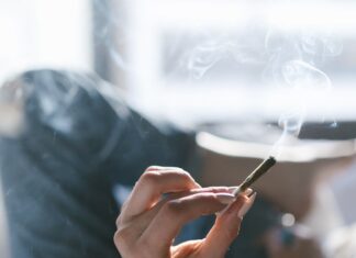 Un estudio de EEUU vincula cannabis con peor sueño objetivo Una persona sostiene un porro encendido mientras permanece tumbada en una cama
