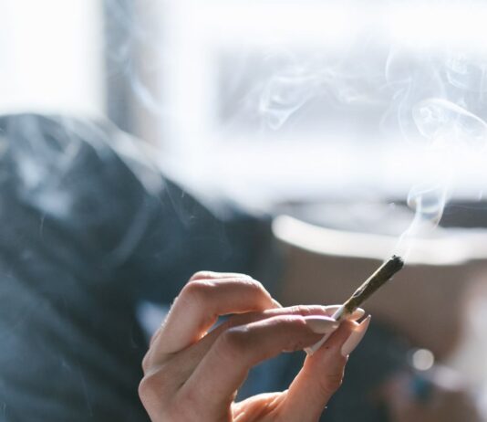 Una persona sostiene un porro encendido mientras permanece tumbada en una cama