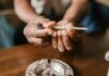 Un ensayo de EE UU relaciona el efecto del cannabis con el sexo y la frecuencia de uso Unas manos sostienen un porro sobre un cenicero situado en una mesa de madera