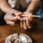 Unas manos sostienen un porro sobre un cenicero situado en una mesa de madera