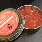 Lata abierta con gominolas rojas de cannabis y su tapa etiquetada sobre una mesa oscura