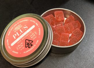 Lata abierta con gominolas rojas de cannabis y su tapa etiquetada sobre una mesa oscura