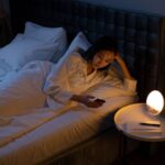 Una mujer mira el móvil en la cama, con la habitación iluminada por una lámpara